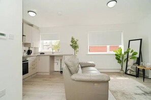 Eine moderne Küche mit weißen Schränken, einem beige farbenen Sofa und einem Blumentopf.