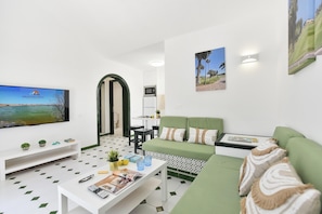 Ein modernes Wohnzimmer mit einem grünen Sofa, einem weißen Couchtisch und einem Flachbildfernseher, der 'VillaGranCanaria' zeigt.