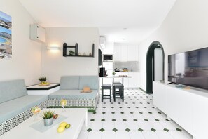 Ein modernes Wohnzimmer mit einer Couch, einem Essbereich mit Tisch und einer Küche mit weißen Schränken.