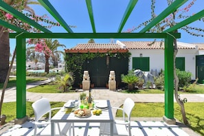 Eine Terrasse im Freien mit Esstisch, umgeben von grünen Säulen und einer Pergola.