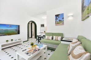 Ein modernes Wohnzimmer mit einem grünen Sofa, einem weißen Couchtisch und einem Flachbildfernseher, der 'VillaGranCanaria' zeigt.