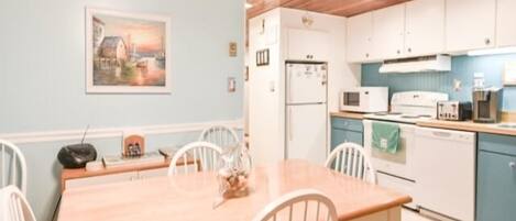A dining area with a wooden table and chairs, a kitchen with white cabinets and appliances, and a ceiling fan.