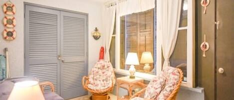 A room with a sofa, two wicker chairs, a table with lamps, a window with curtains, and a door with a keyhole.