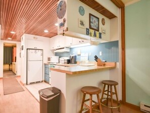 A kitchen with a wooden ceiling, white cabinets, a refrigerator, a sink, and two stools. - Direct ocean front 1 BR and Den, Pool, Parking, WiFi Beautifully Decorated (Ocean City)