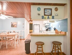 A kitchen with a wooden ceiling, a bar area with stools, and a dining area with chairs and a table. - Direct ocean front 1 BR and Den, Pool, Parking, WiFi Beautifully Decorated (Ocean City)