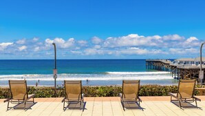 Vista de playa con sillas, un muelle y cielo despejado.