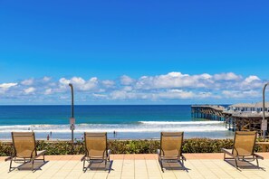 Blick auf einen Strand mit Stühlen, einem Steg und blauem Himmel.