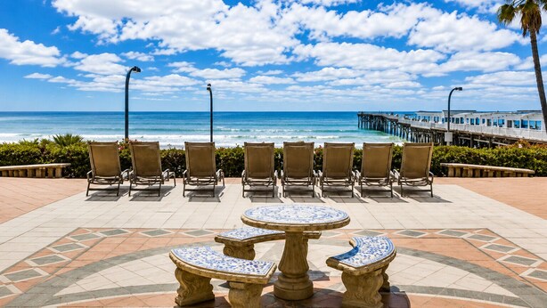 Un patio frente a la playa con sillas y una mesa, con vista al océano y un muelle.