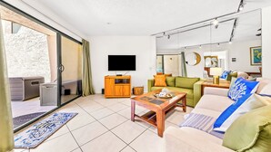 Una sala de estar con sofá, mesa de centro, televisor y puerta corrediza de vidrio que da a un área exterior.