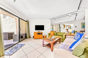 Ein Wohnzimmer mit einer Couch, einem Couchtisch, einem Fernseher und einer Schiebetür zu einem Außenbereich.