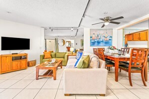 Ein Wohnzimmer mit einer Couch, Couchtisch, Fernseher, Holzschrank und einem Essbereich mit Stühlen und Tisch.