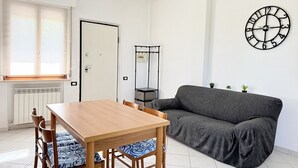 Ein Zimmer mit einem Holztisch, einer grauen Couch, einer Wanduhr und einer Heizung.