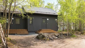 A cabin with a dark exterior, wooden steps, and a metal roof, surrounded by trees. - Room-cozy City Cottage With Sauna, hot t (Espoo)