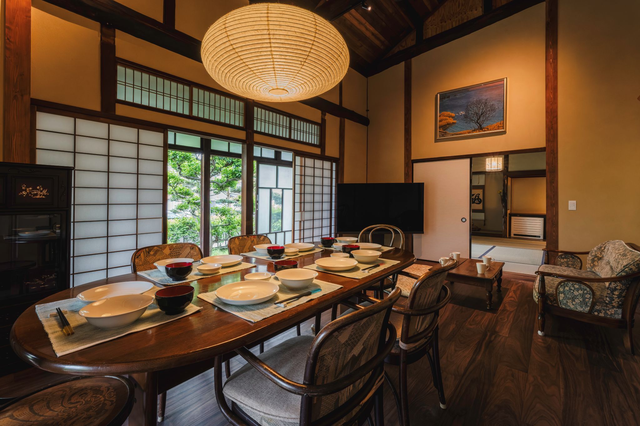 Een traditionele Japanse eetzaal met tatami matten, een lage tafel gedekt voor een maaltijd, en een groot raam met uitzicht op groen.