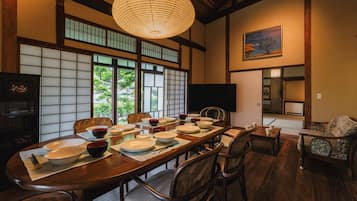 Een traditionele Japanse eetzaal met tatami matten, een lage tafel gedekt voor een maaltijd, en een groot raam met uitzicht op groen.