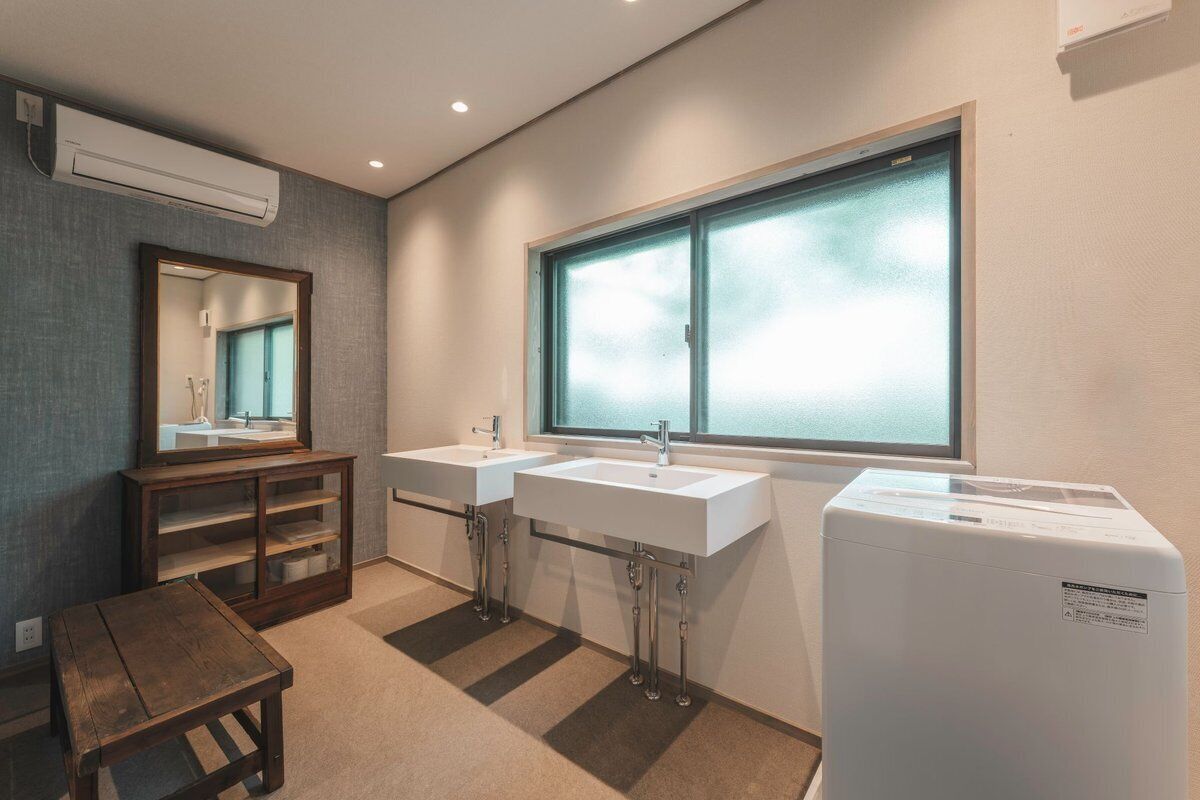 A bathroom with two sinks, a mirror, a window, and a small table.