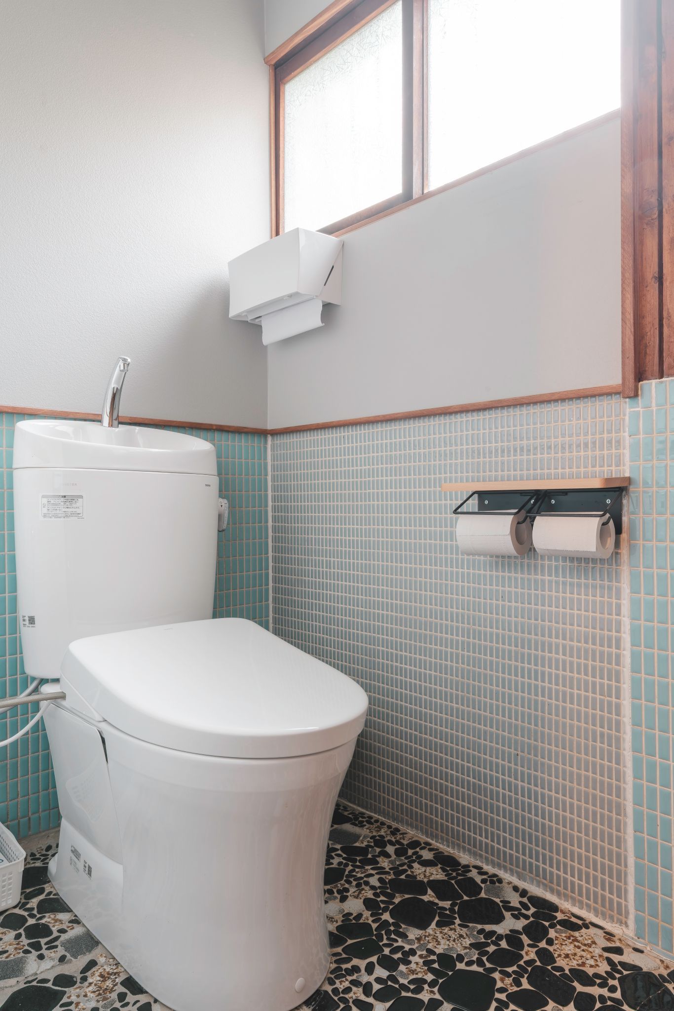A bathroom with a white toilet, a sink, a window, and a toilet paper holder.