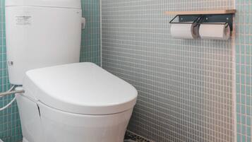 A bathroom with a white toilet, a sink, a window, and a toilet paper holder.