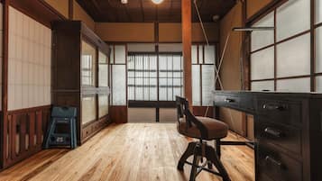 Una habitación con piso de madera, un escritorio con cajones, una silla y un ventanal con persianas.