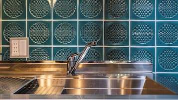 Un lavamanos de acero inoxidable con un grifo moderno, un escurreplatos perforado y una pared con mosaicos circulares.