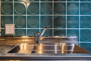 Ein Spülbecken aus Edelstahl mit modernem Wasserhahn, einem Sieb und einer Wand mit runden Mosaikfliesen.
