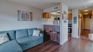 Un saló modern amb un sofà, una cuina amb armaris i electrodomèstics, i un passadís que condueix a una altra habitació.