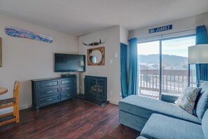 A living room with a TV, fireplace, and a view of a town. - Condo close to hiking trails and base area (Angel Fire)