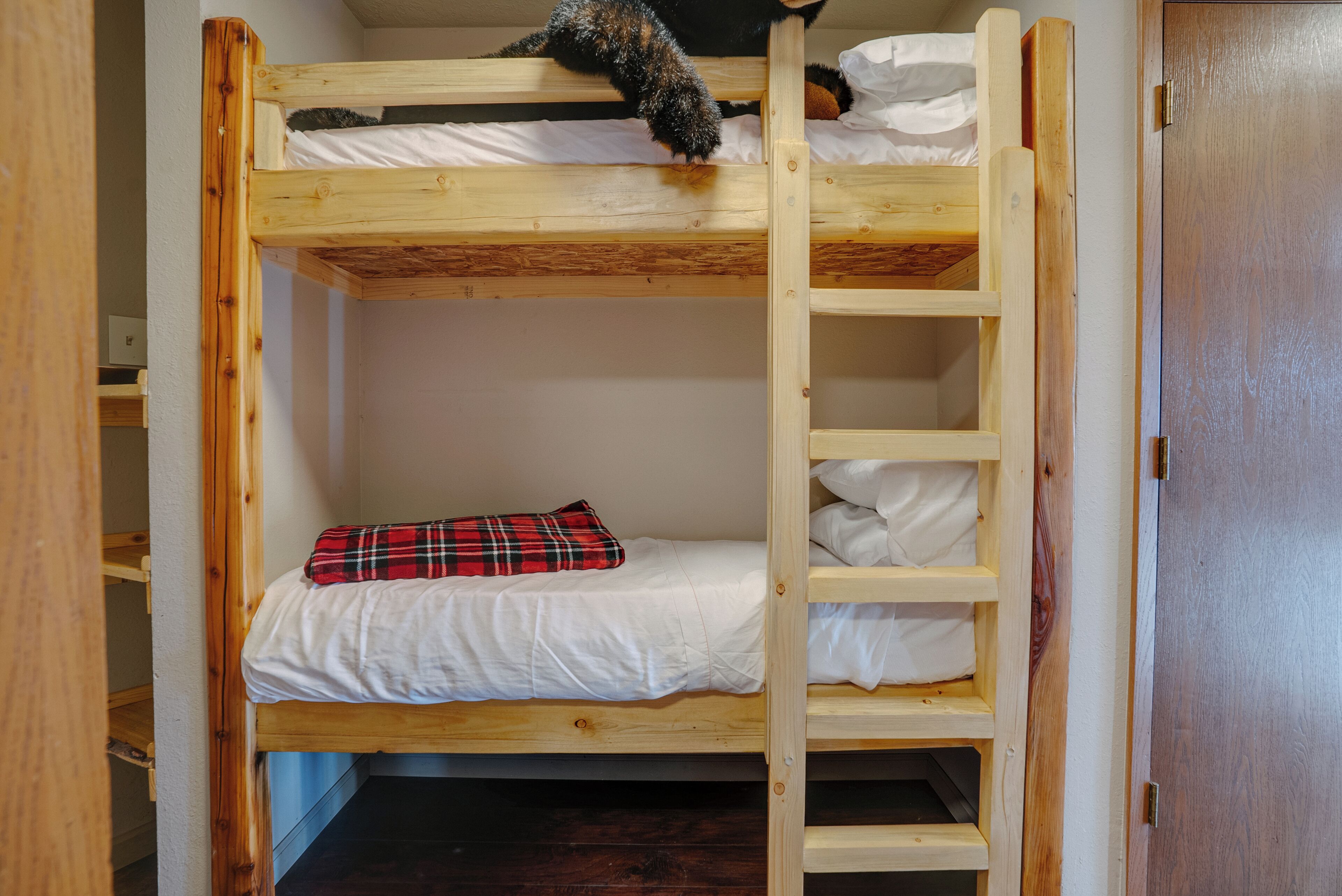 Una cama litera con escalera, un cojín de cuadros y una puerta de madera.