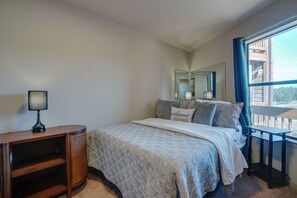 A bedroom with a bed, a bedside table, a lamp, a mirror, and a window with a view of a balcony. - Condo close to hiking trails and base area (Angel Fire)
