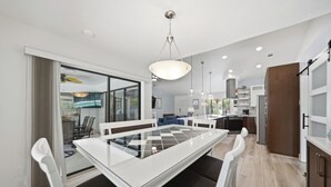 Une cuisine moderne dotée d’un îlot central, d’un coin repas avec une table à plateau en verre, et d’une vue sur l’espace de vie, accessible par une porte vitrée.