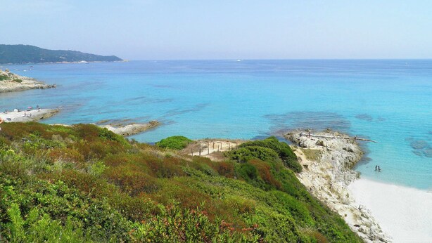 Paisaje costero con aguas turquesas cristalinas, costas rocosas y una playa arenosa.