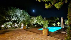 Una piscina con borde de baldosas, rodeada de árboles y una valla.