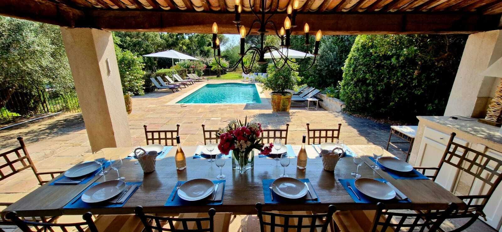 An outdoor dining area with a pool in the background.