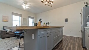 A modern kitchen with grey cabinets, a wooden countertop, and a built-in island. There is a ceiling fan, a refrigerator, and a dining area with a sofa and table. - Downtown Lehighton Just a 5 min drive to Jim Thorpe! (Lehighton)