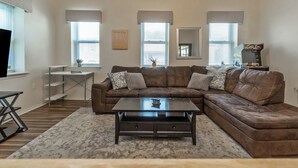 A living room with a brown sectional sofa, a coffee table, a TV, and a gaming console. - Downtown Lehighton Just a 5 min drive to Jim Thorpe! (Lehighton)