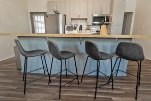 A kitchen with four bar stools, a refrigerator, a microwave, and a sink.