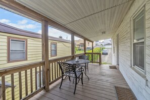 A covered porch with a table and chairs, wooden railings, and a view of neighboring houses.