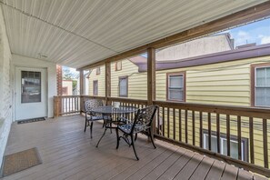 En overdækket veranda med træterrasse, metalstole og et bord.