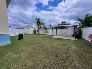 A backyard with a covered patio, a white fence, and a palm tree.