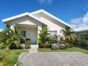 A two-story house with a front porch, a small garden with various plants and flowers, and a clear blue sky.