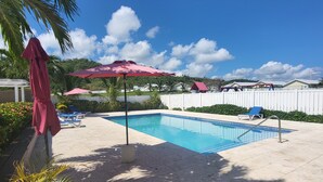 Une piscine entourée de chaises longues, de parasols et d’une clôture blanche en arrière-plan.