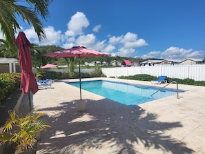 A swimming pool with lounge chairs, umbrellas, and a white fence in the background.