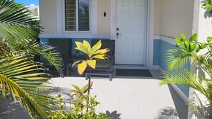 Une maison avec une porte blanche, une fenêtre à carreaux et un petit porche agrémenté de plantes.