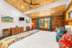 Ein Schlafzimmer mit einem großen Bett, Holzboden, einem Fernseher und einem Fenster mit Vorhängen.