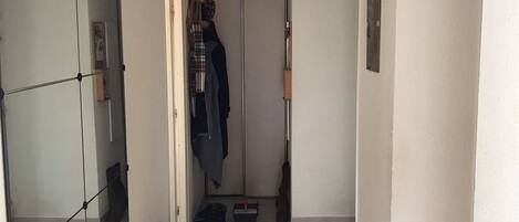 A hallway with a mirror, a coat rack, a wooden bench with shoes, and a door leading to another room.