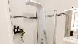 Ein modernes Badezimmer mit einer gläsernen Duschkabine, einem weißen Waschbecken und einem Spiegel darüber.
