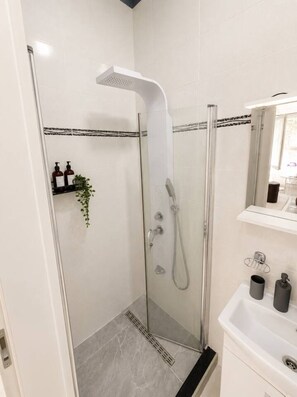 A modern bathroom with a glass-enclosed shower, a white sink, and a mirror above it. - Cozy Boho Studio with Kitchenette & Bath (Bucharest)