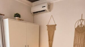 Ein Schlafzimmer mit Bett, Kissen, Nachttisch, Lampe, Wandbehagung aus Makramee und einem Kleiderschrank.