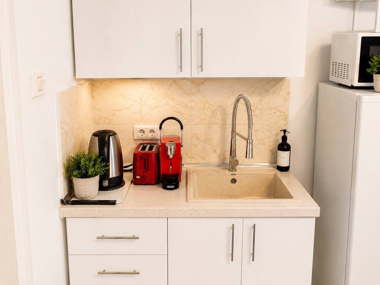 A kitchen with a sink, white cabinets, a toaster, a kettle, and a microwave.