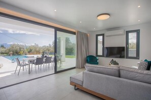 Ein modernes Wohnzimmer mit Sofa, Fernseher und einem Essbereich mit Stühlen und Tisch.